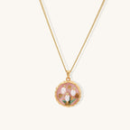Gold-plated pendant necklace with pink enamel background and white freshwater pearl floral design on neutral background.