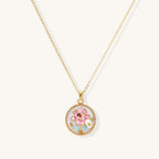 Gold-plated circular pendant featuring pink enamel rose with pearl accents and green leaf details on adjustable chain.