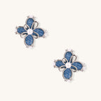 Blue denim flower stud earrings with silver framework, white pearl centers, and crystal accents on cream background.