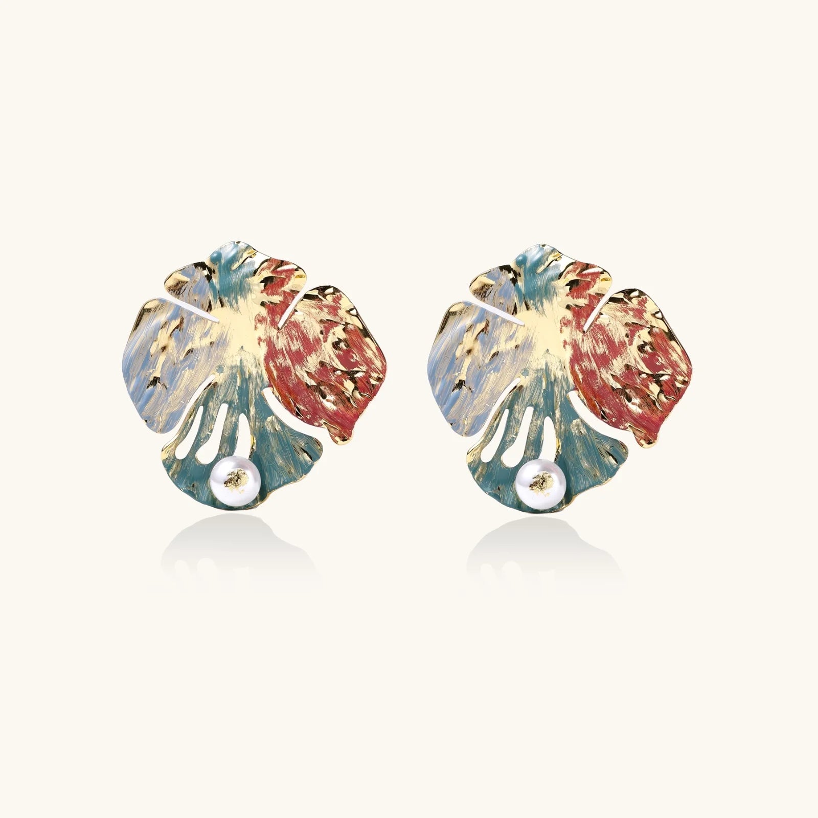 Artistic monstera-shaped earrings with teal, coral, and cream enamel brushstrokes, gold trim, and white pearl accent