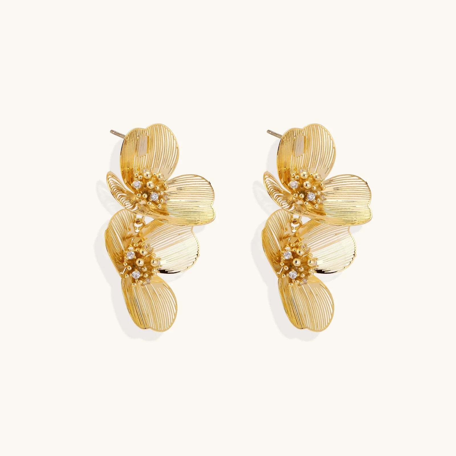 Pair of gold-plated double flower earrings with textured petals and crystal centers on cream background.