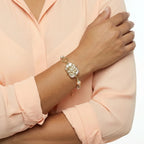 Close-up of a hand wearing a decorative bracelet on a light pink shirt.