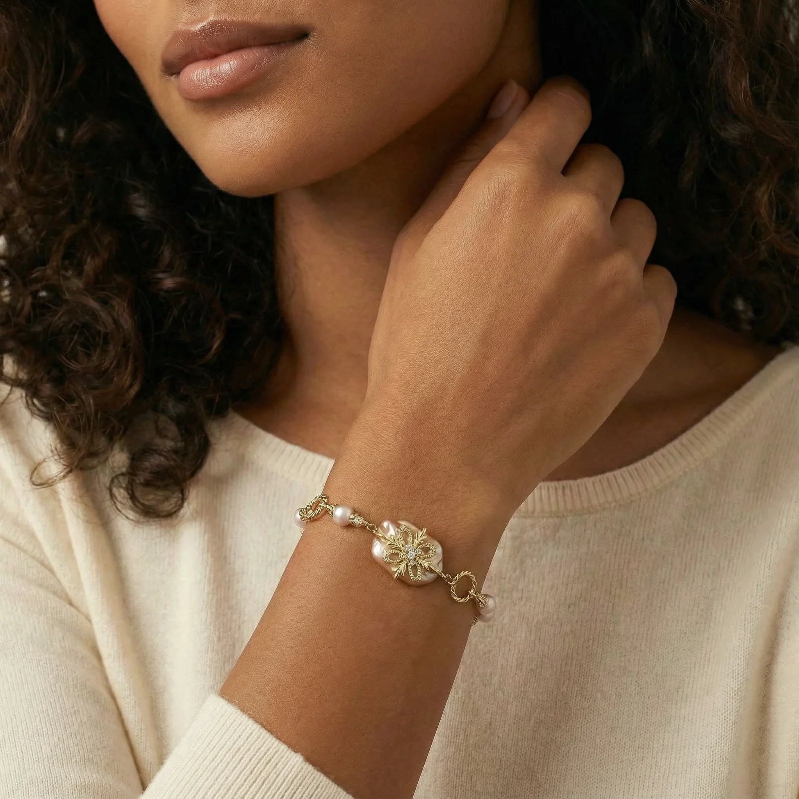 Woman wearing a gold bracelet with a floral design on her wrist.