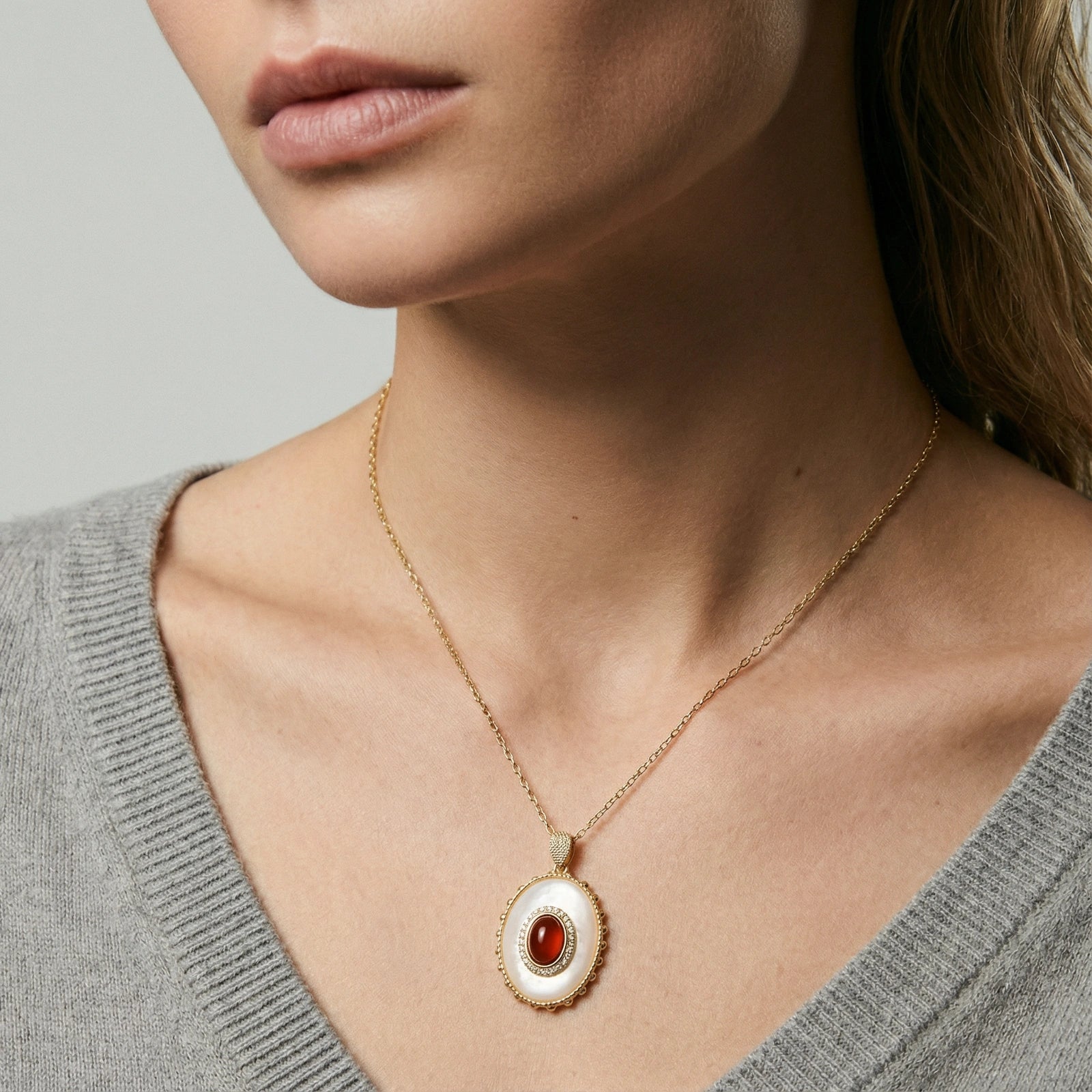 Close-up of a person wearing a gold necklace with a red stone pendant on a neutral background