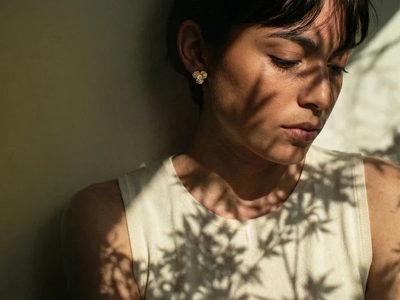 Woman with a serious expression, wearing a white sleeveless top, with shadows of leaves on her face.