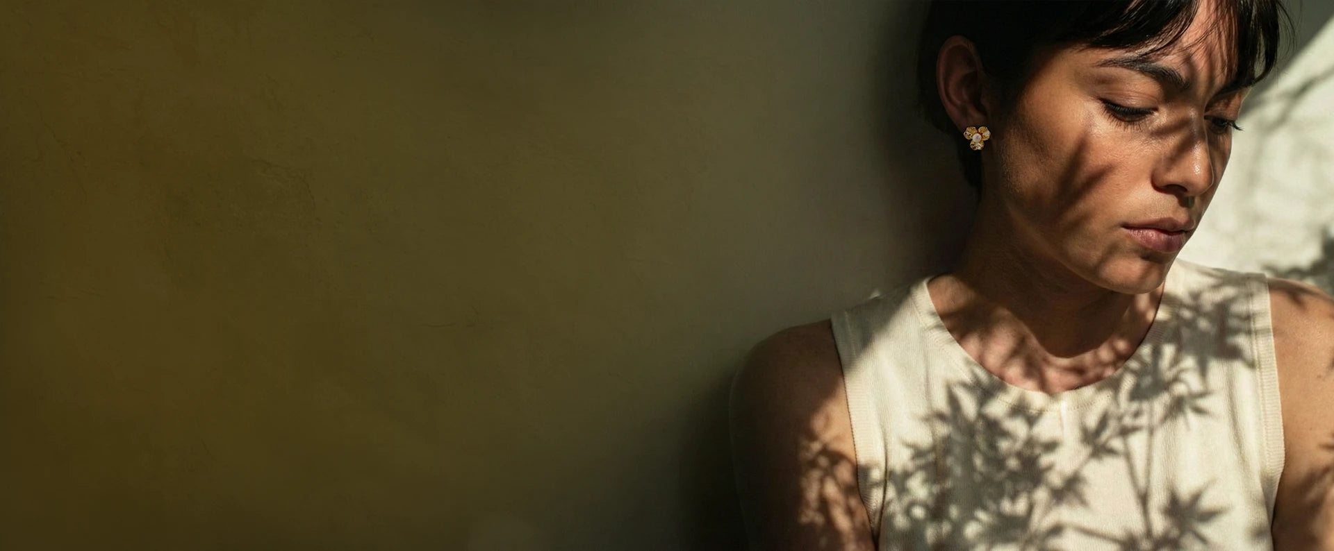 Person with a shadow of leaves on their face against a plain background