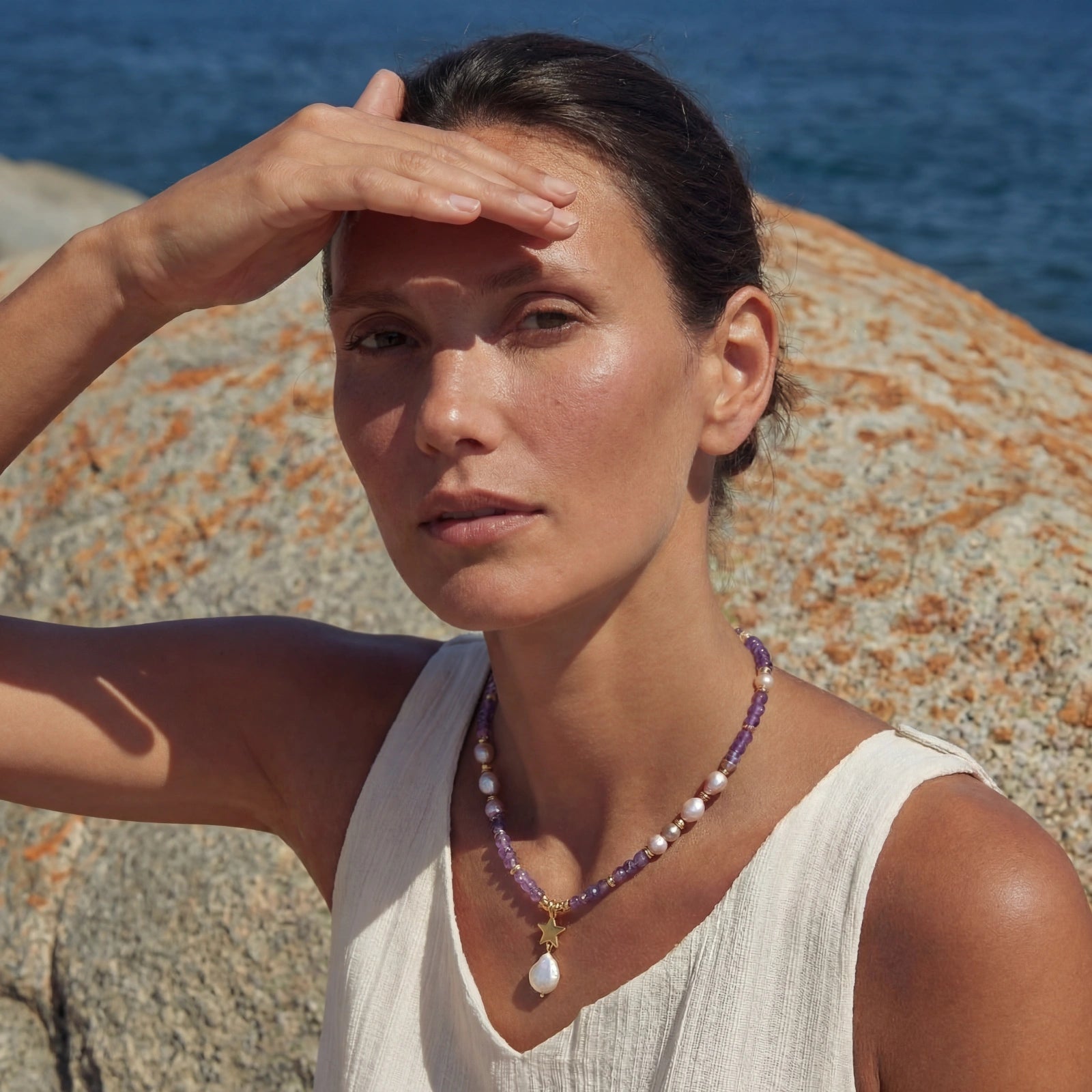 Woman on a rocky beach with ocean view, wearing a necklace.