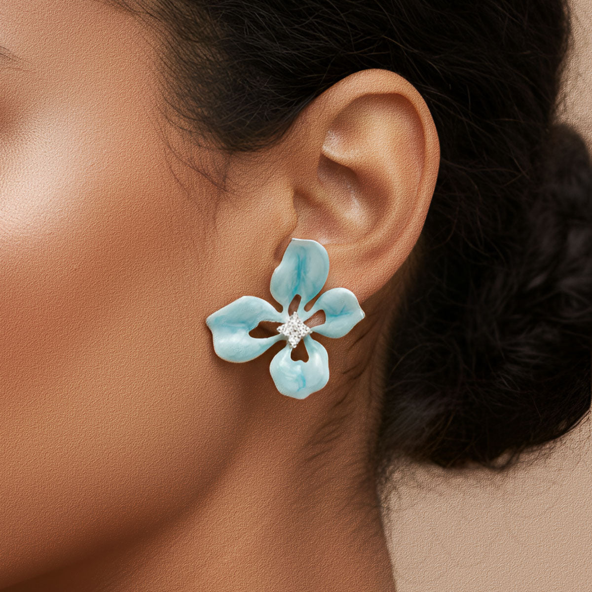 Close-up of a woman wearing a turquoise flower-shaped earring with a clear gemstone.