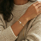 Gold bracelet with a small butterfly charm on a person wearing a beige sweater.
