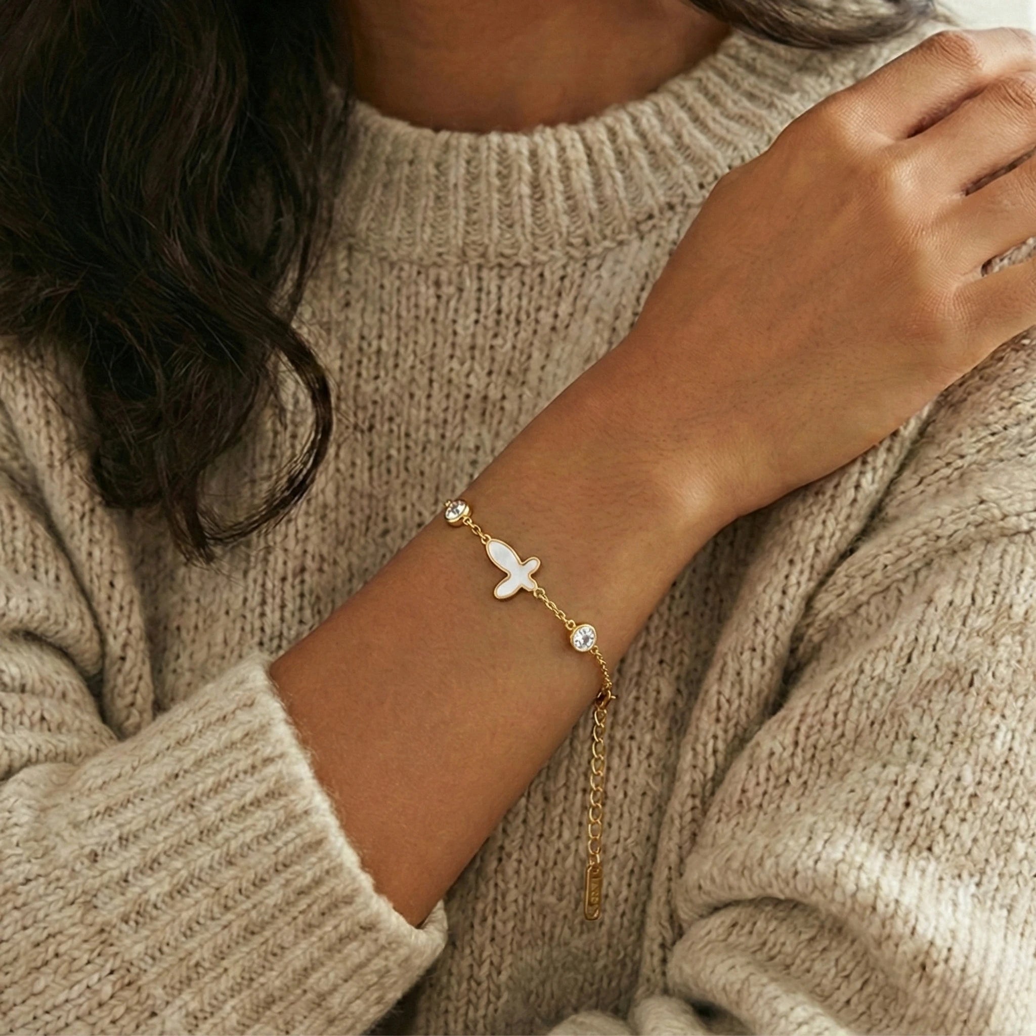 Gold bracelet with a small butterfly charm on a person wearing a beige sweater.