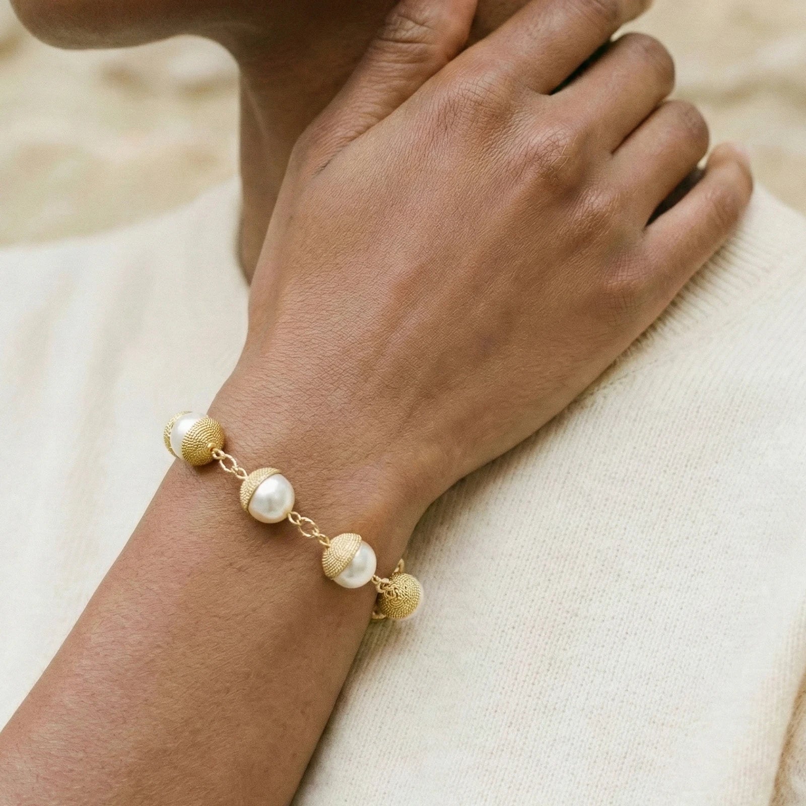 Gold and pearl bracelet on a wrist against a neutral background
