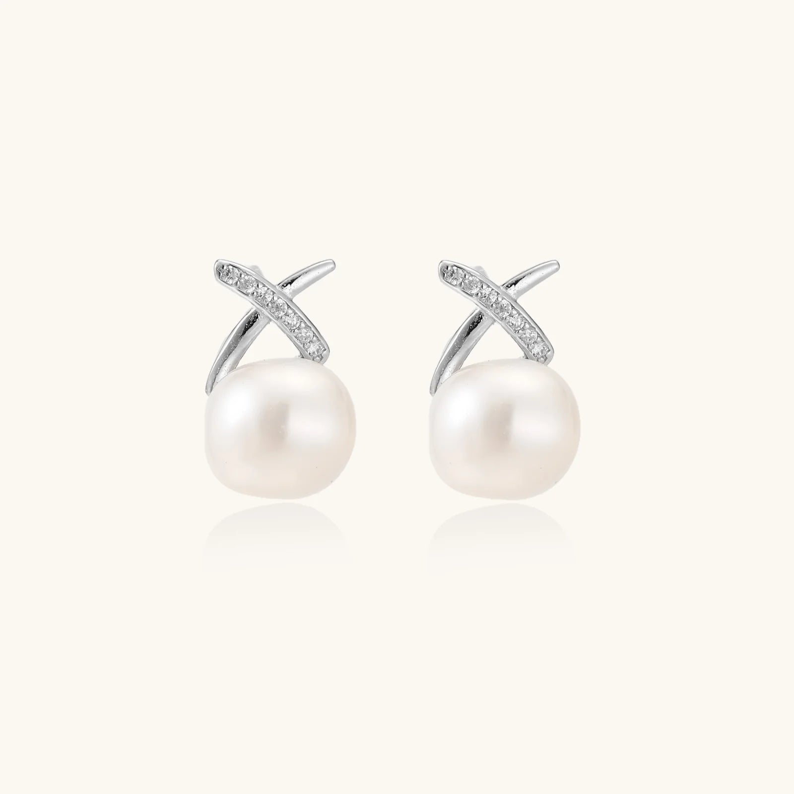 Rhodium-plated silver stud earrings with sparkling X design above lustrous round freshwater pearls on white background. 2