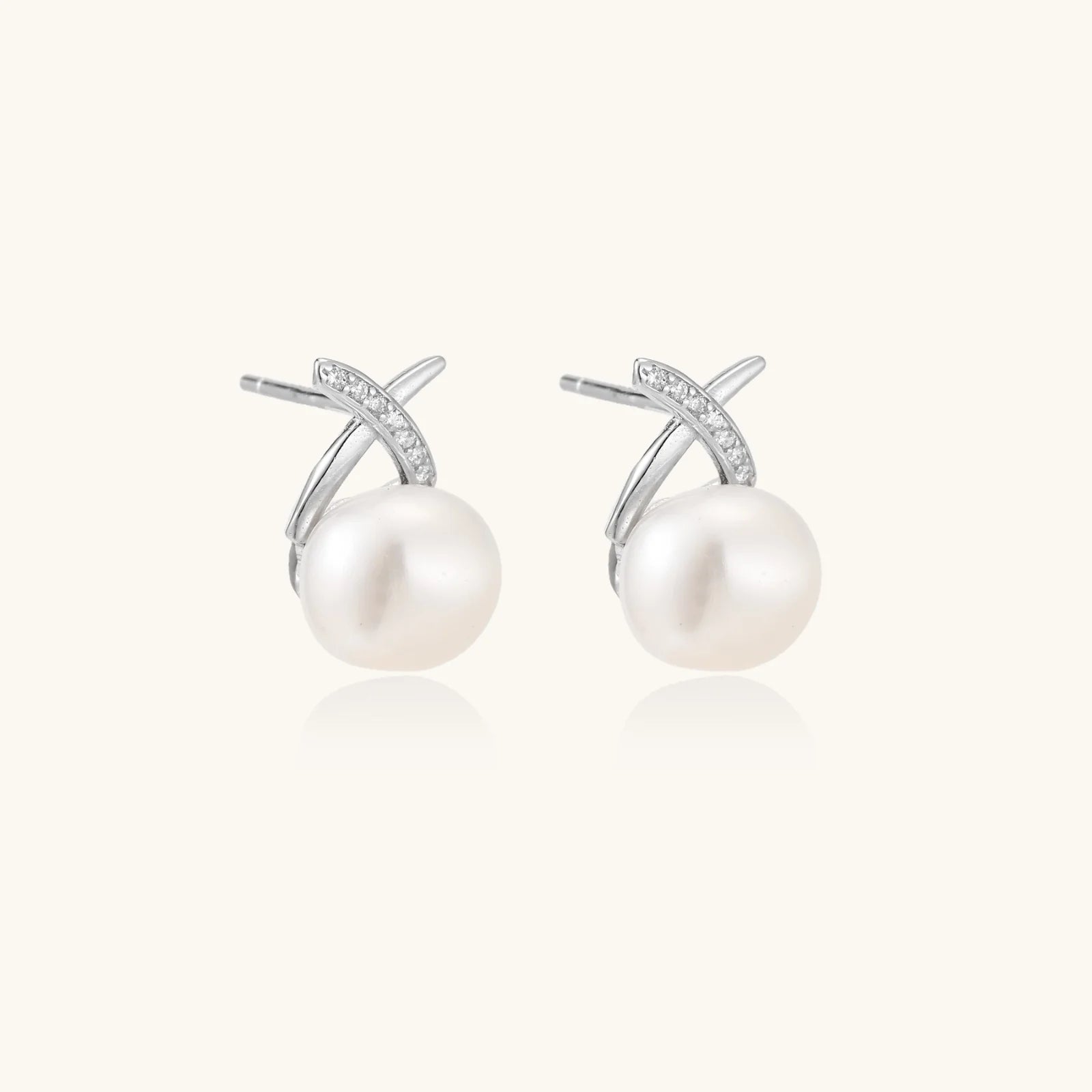 Rhodium-plated silver stud earrings with sparkling X design above lustrous round freshwater pearls on white background. 3