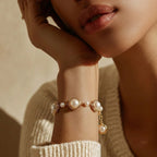 Close-up of a person wearing a pearl bracelet on a neutral background
