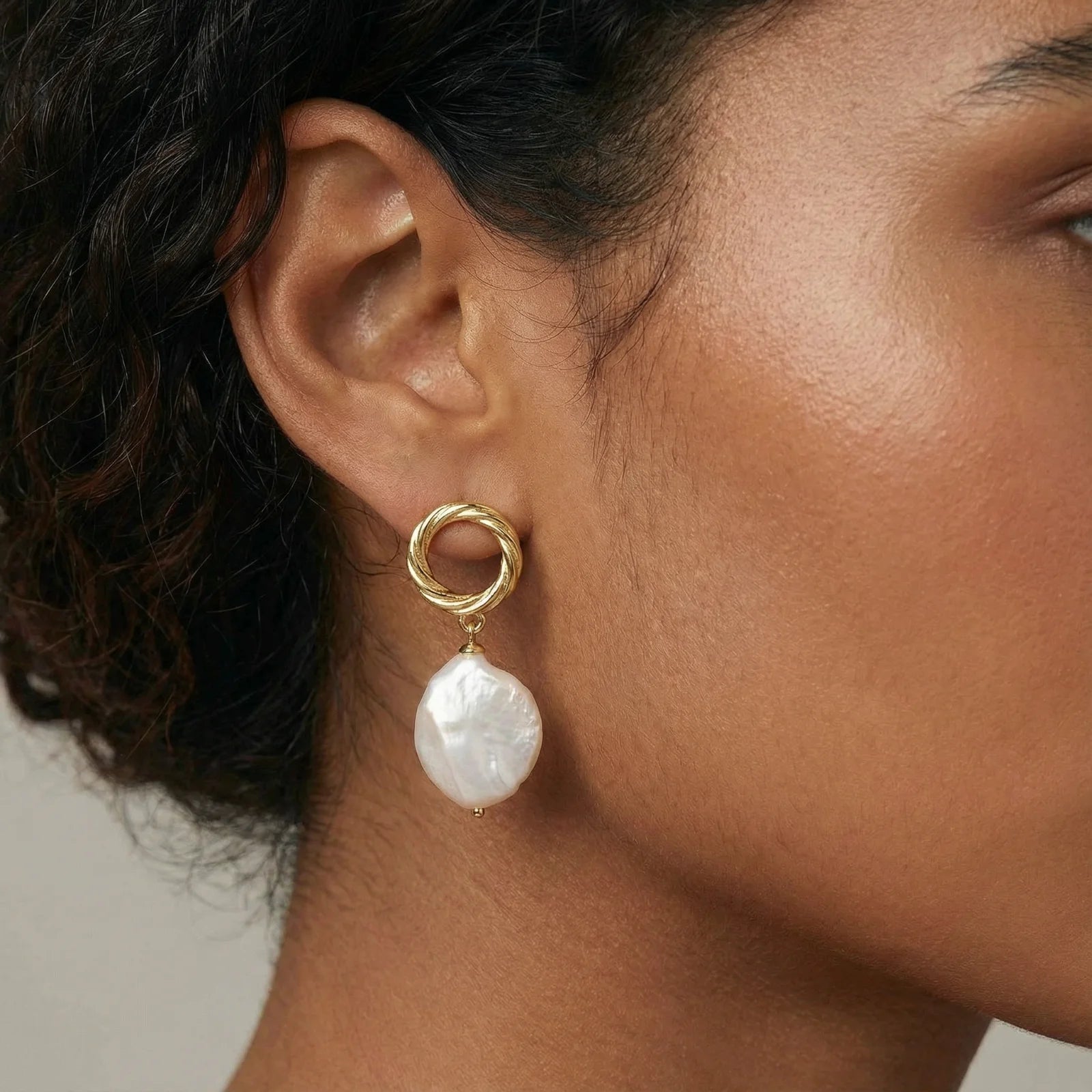 Close-up of a person wearing a gold earring with a baroque pearl drop.