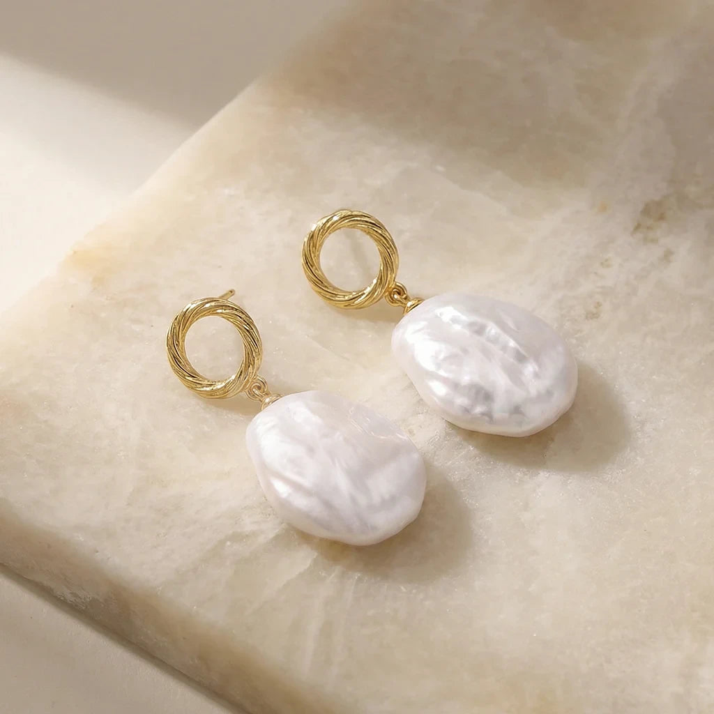 Pearl earrings with gold hooks on a beige stone surface