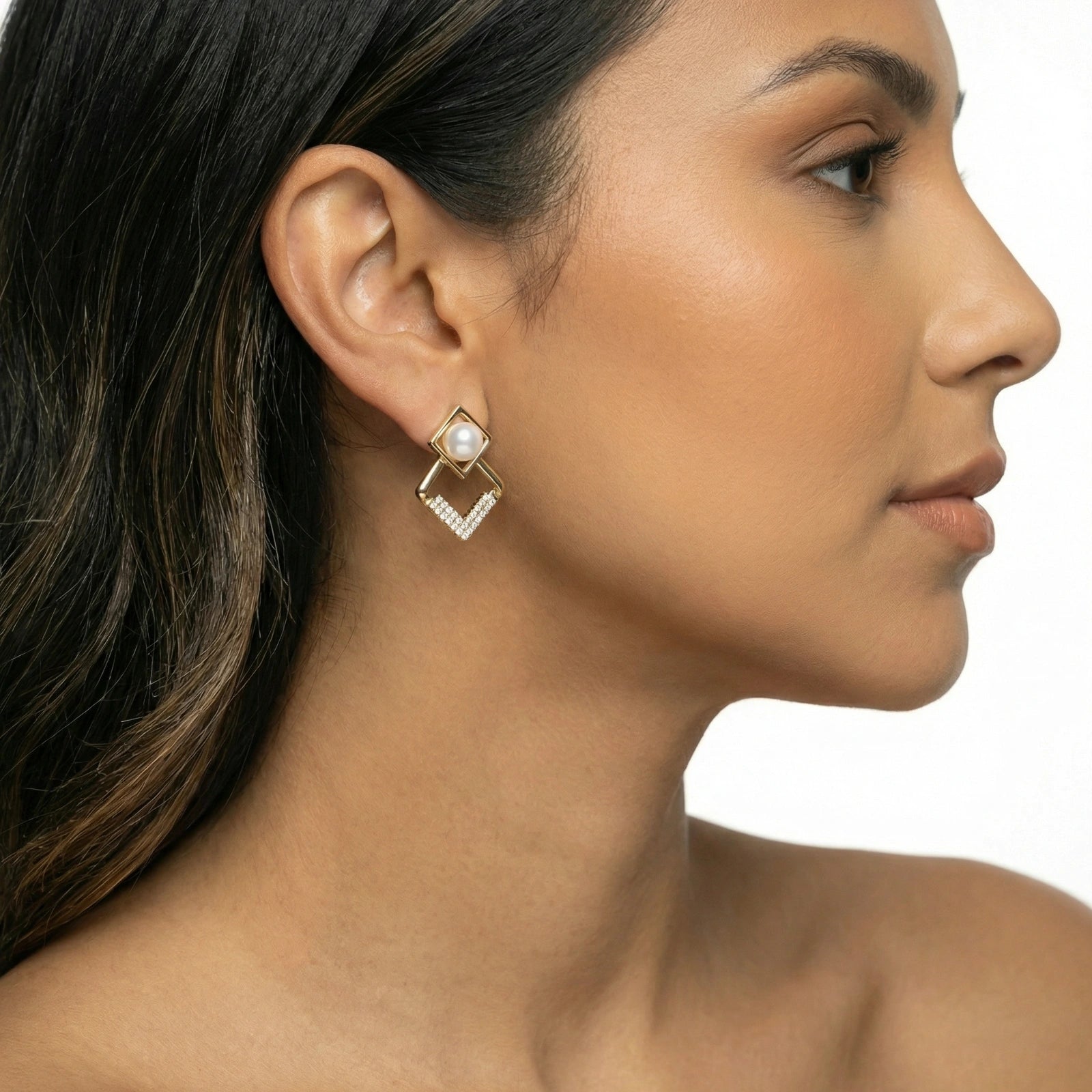 Close-up of a woman wearing a gold earring with a pearl on a white background