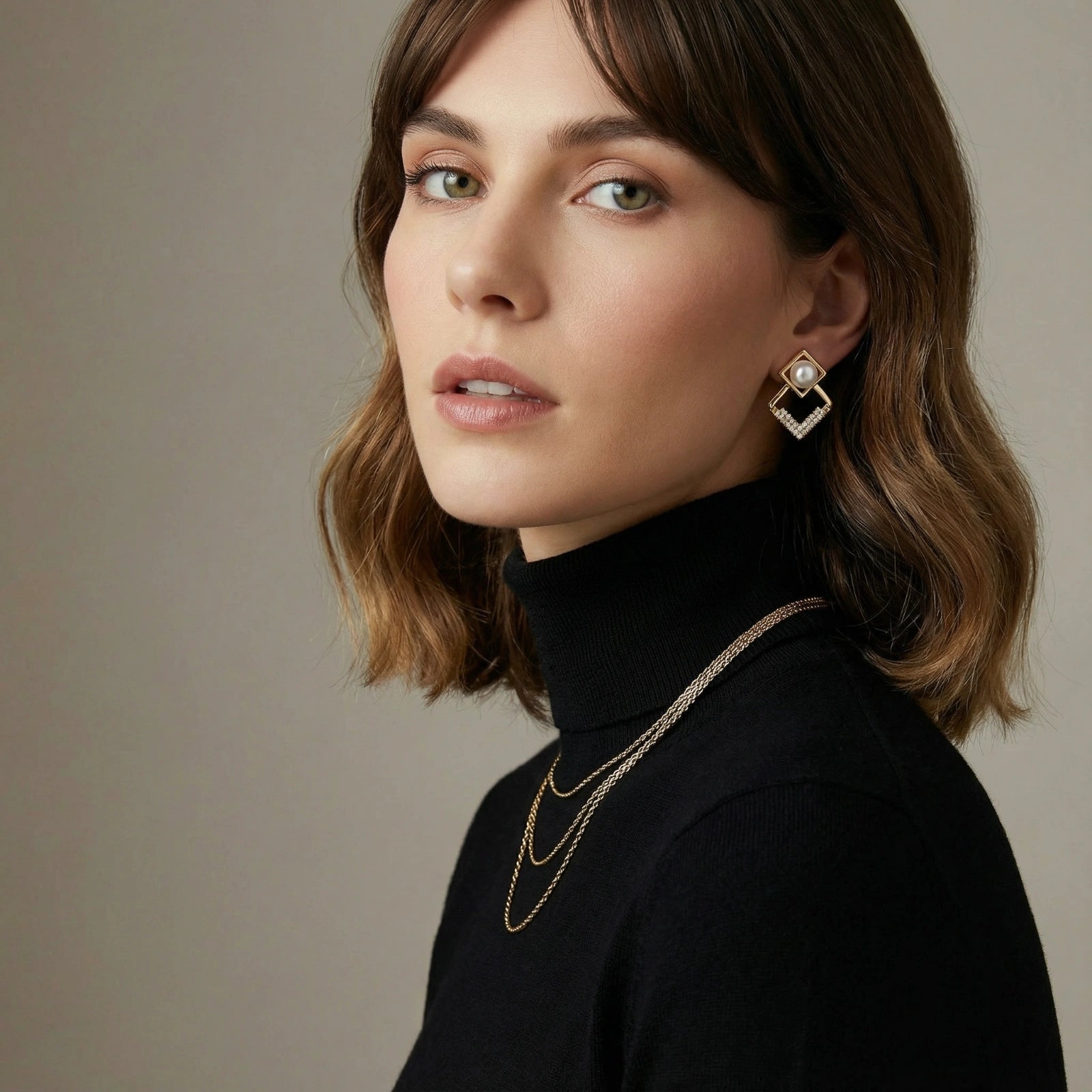 Woman wearing geometric gold jewelry against a neutral background
