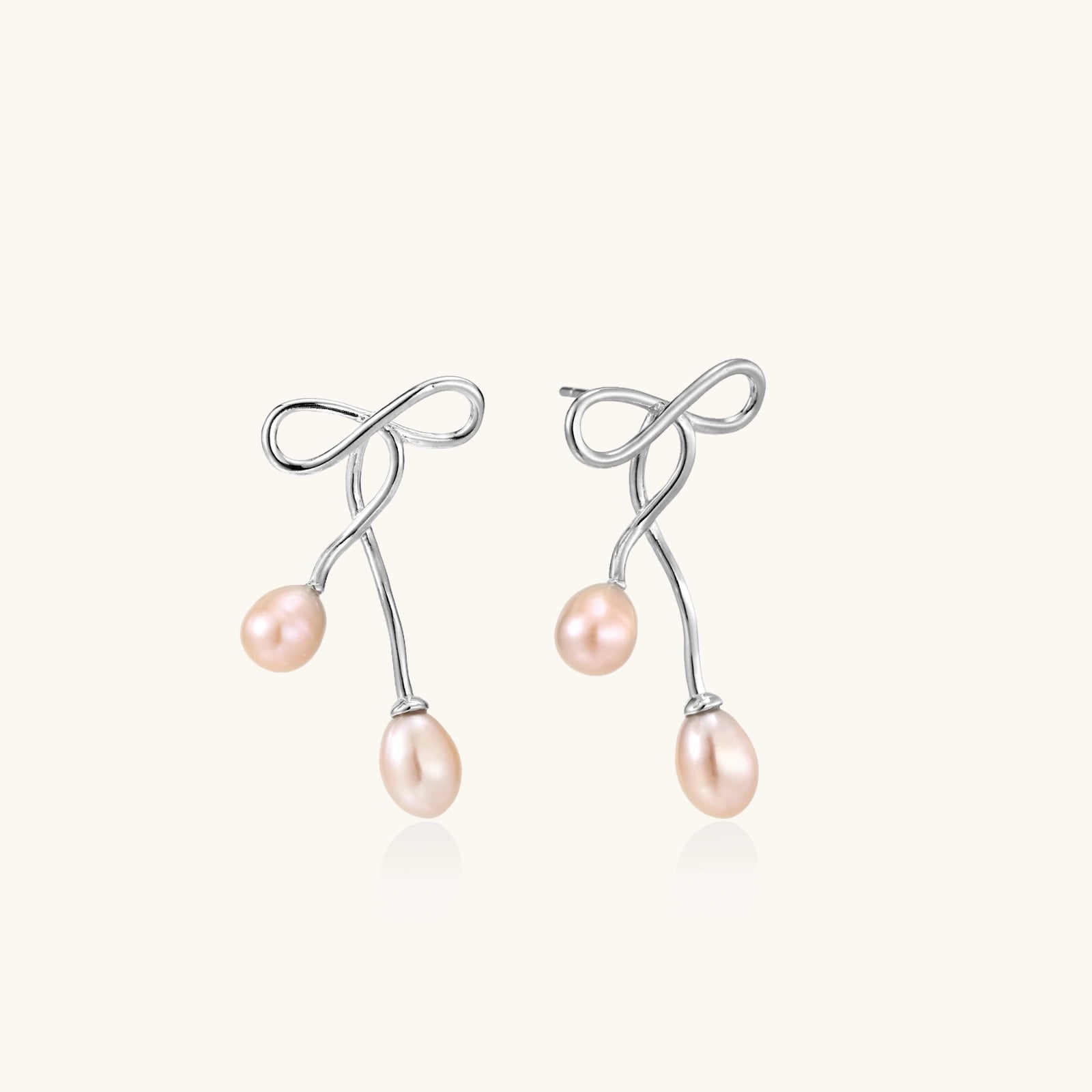 Pair of silver earrings shaped like a ribbon with pink pearls on a white background