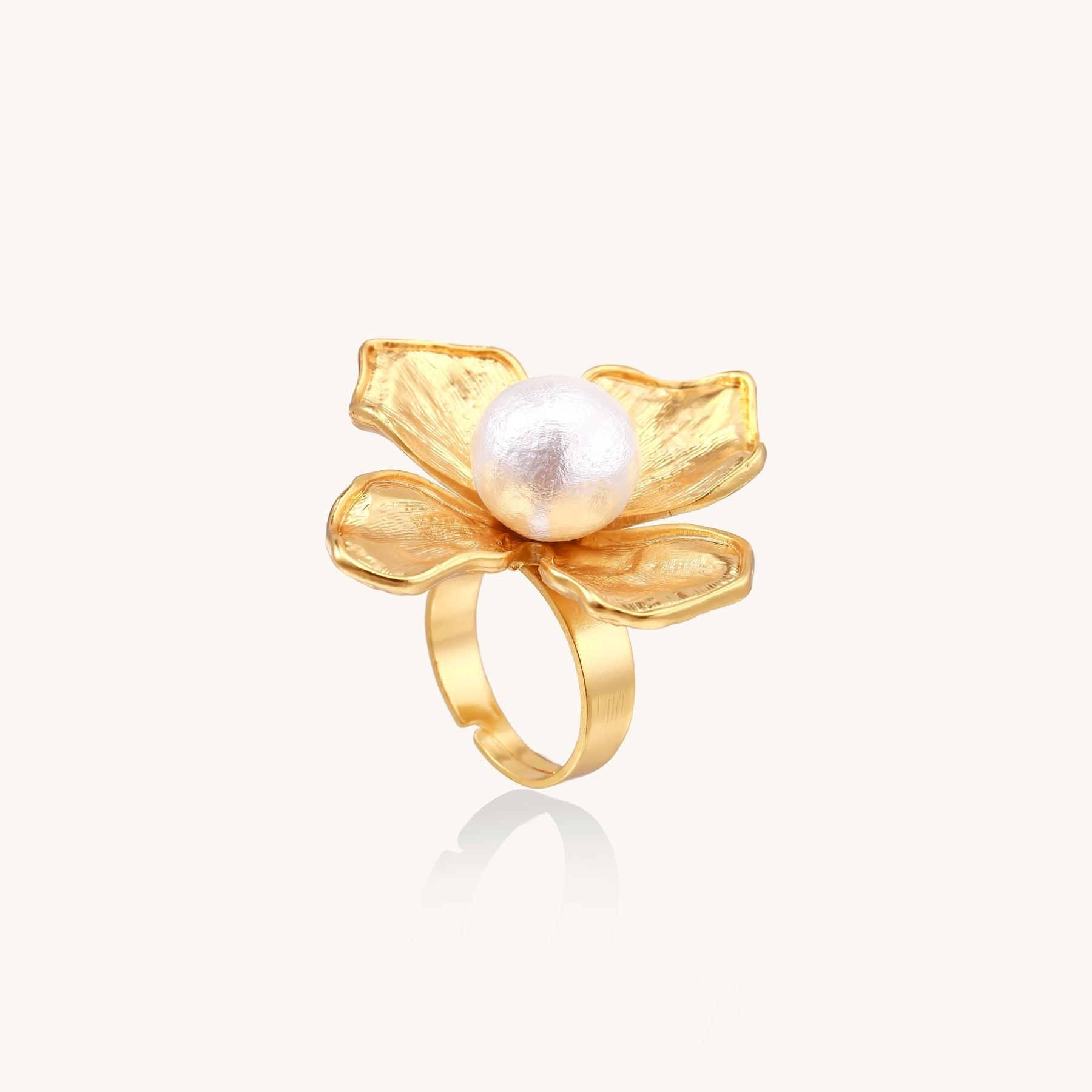 Gold ring with dimensional 4-petal flower design and white cotton pearl center on neutral background
