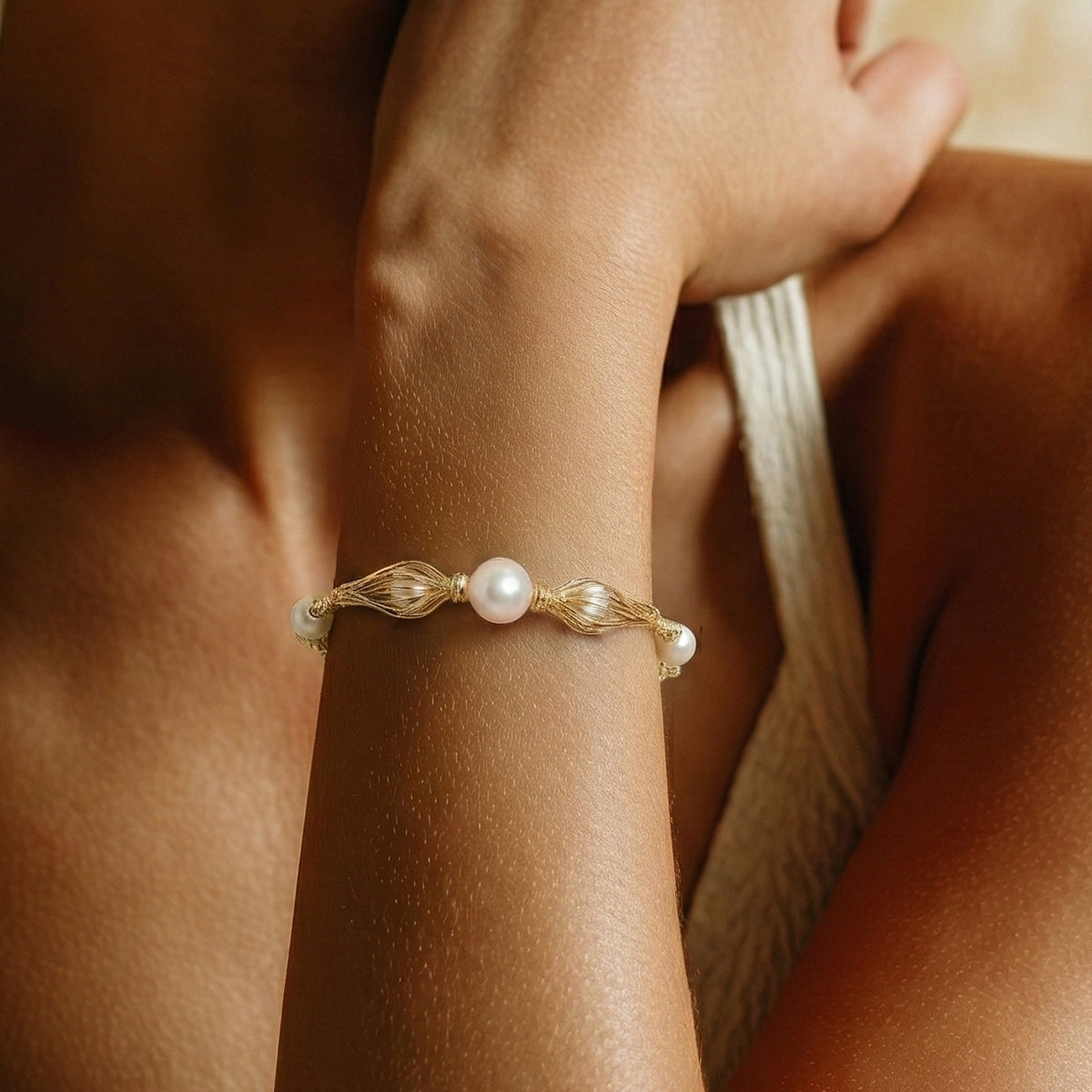 Gold bracelet with pearls on a wrist against a blurred background