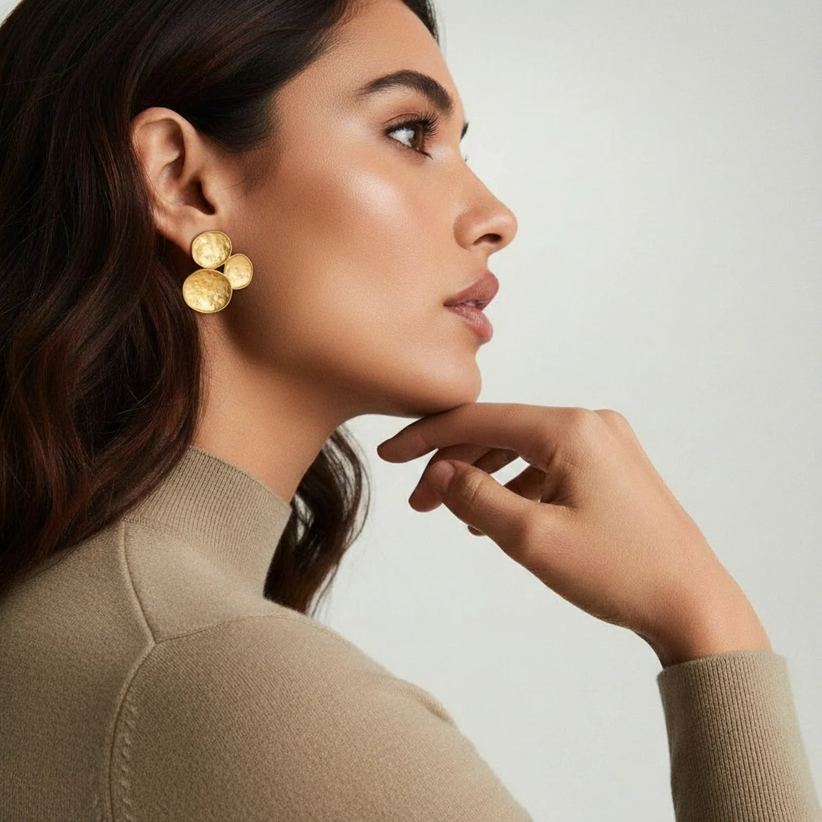 Woman wearing gold earrings with a neutral background