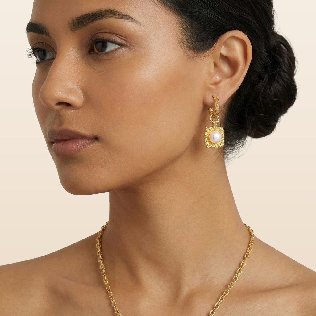 Woman wearing hammered gold earrings with a pearl against a beige background