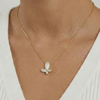 Gold necklace with a butterfly pendant worn by a person against a neutral background