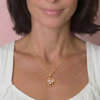 Woman wearing a gold necklace with a floral pendant against a pink background