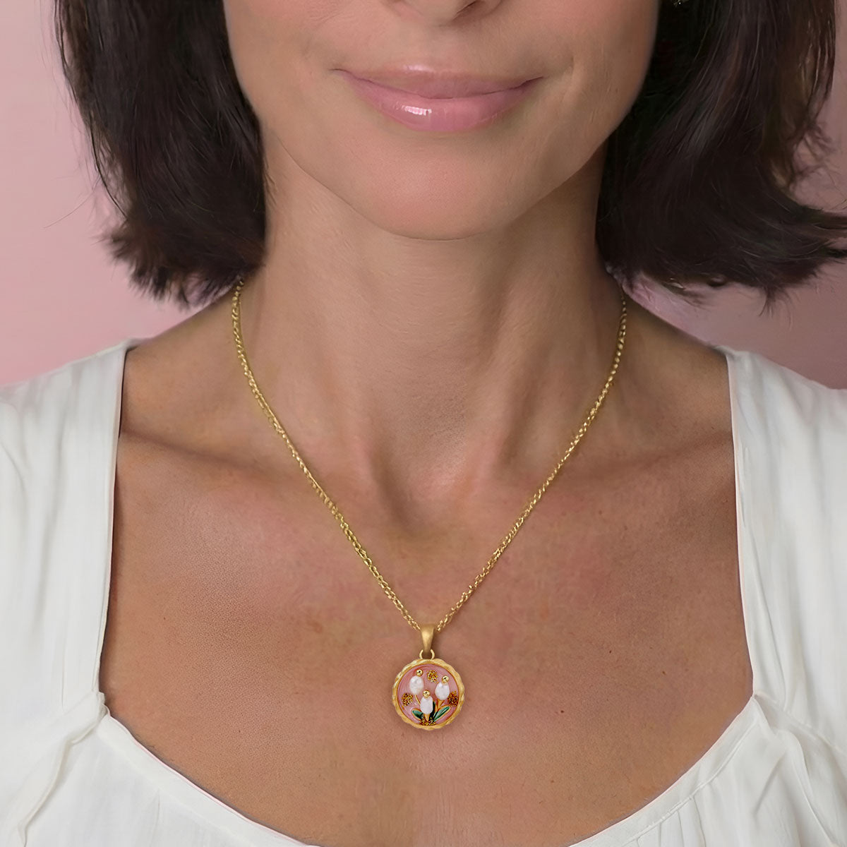 Woman wearing a gold necklace with a floral pendant against a pink background