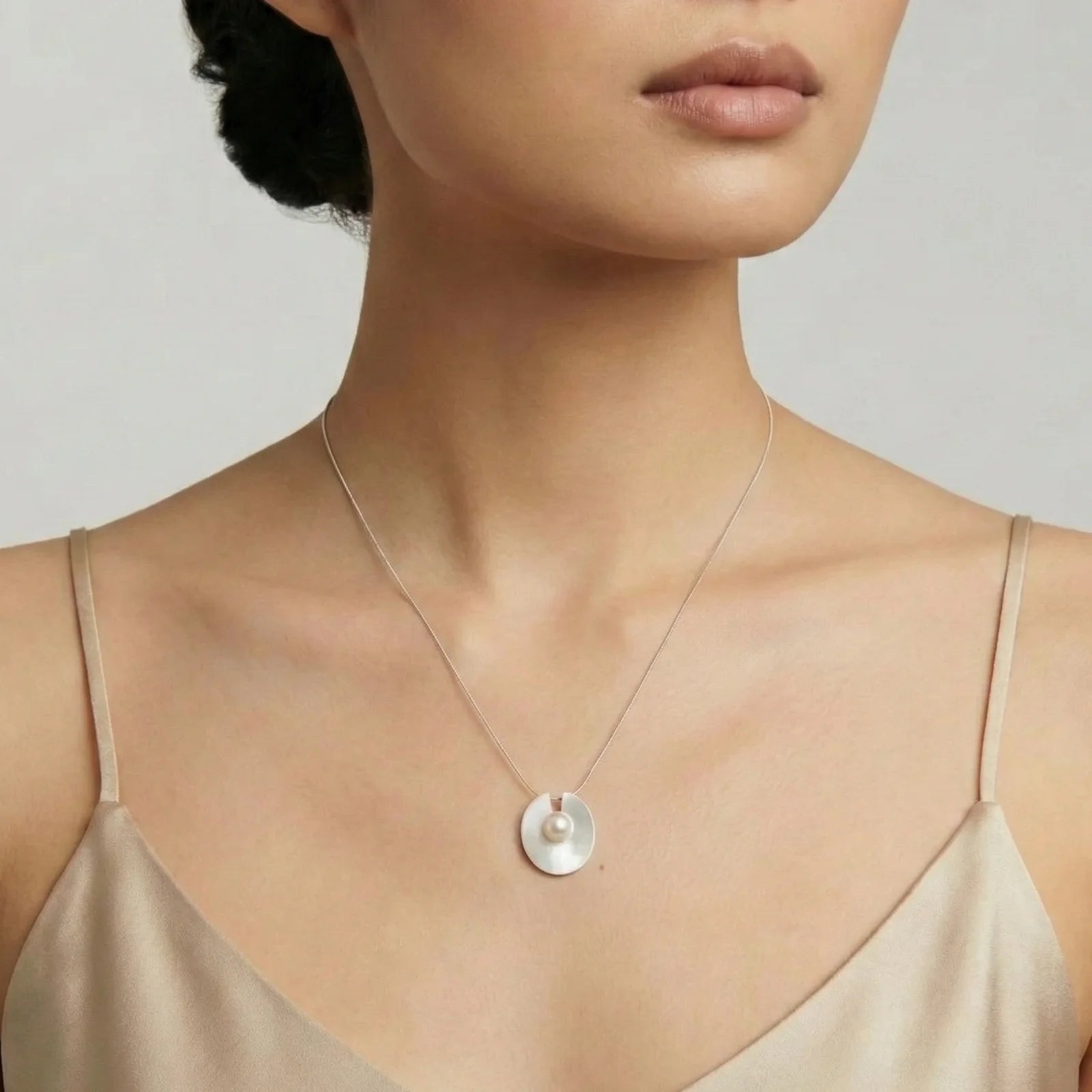 Woman wearing a delicate necklace with a circular pendant against a neutral background