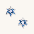 Pair of maple-leaf-shaped earrings with denim fabric and pearls on a white background