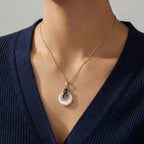 Gold necklace with a pendant worn by a person in a navy blue top against a gray background