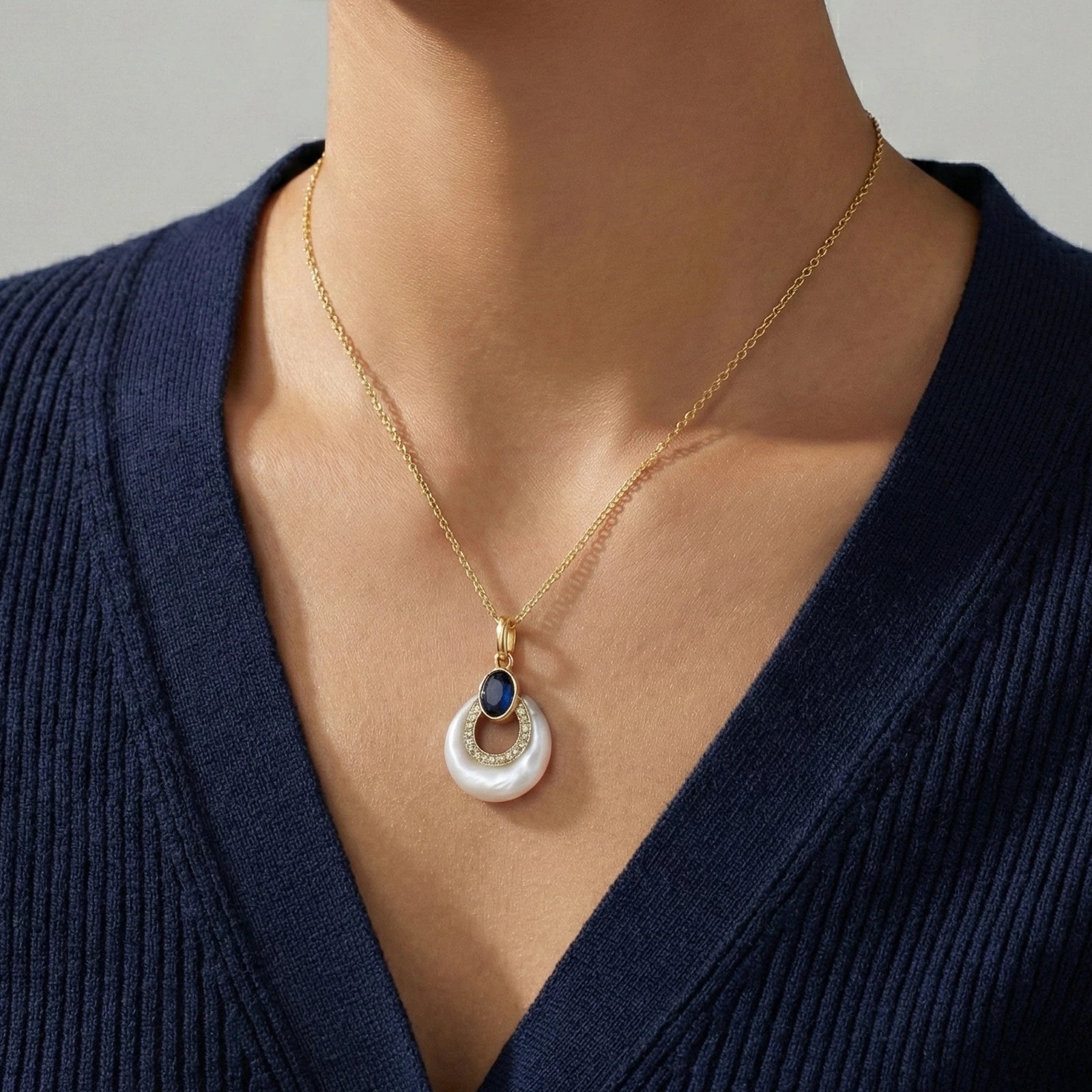 Gold necklace with a pendant worn by a person in a navy blue top against a gray background