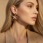 Close-up of a woman wearing gold floral earrings with a neutral background