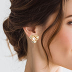 Close-up of a woman wearing gold floral earrings with a pearl center.