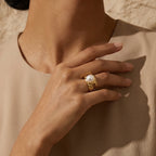 Hand wearing a textured gold ring with a pearl on a beige background