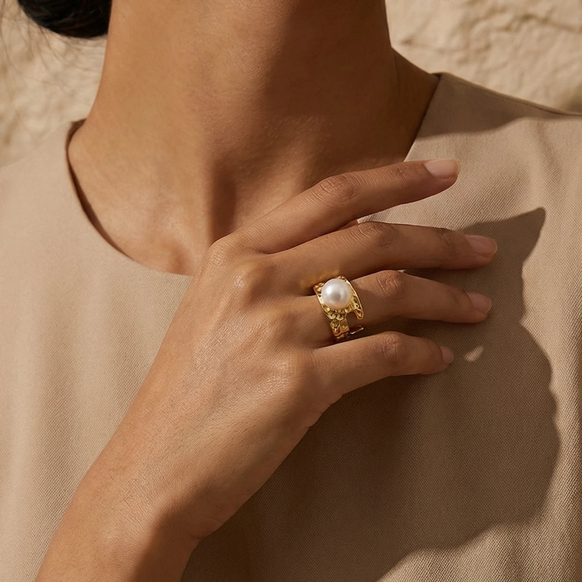 Hand wearing a textured gold ring with a pearl on a beige background