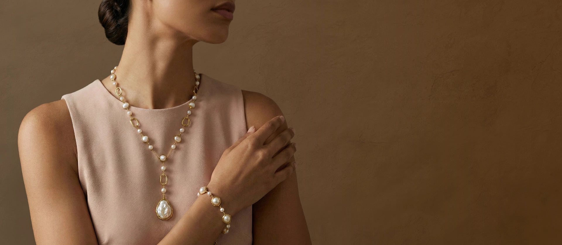 Woman wearing a pearl necklace and bracelet against a brown background