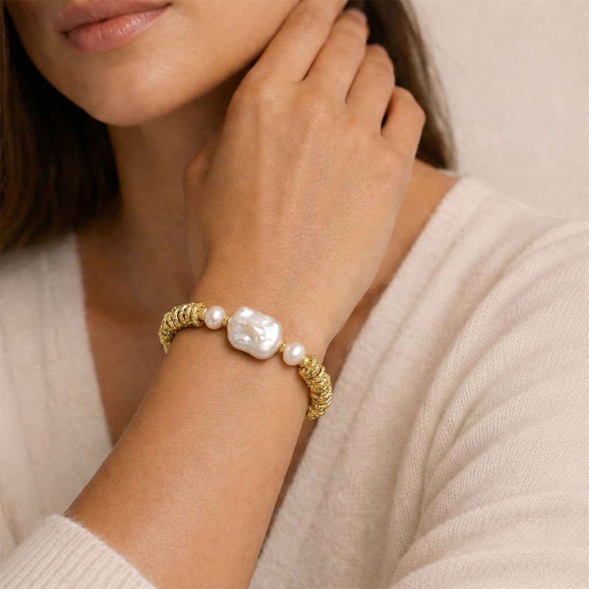 Gold bracelet with pearls on a person wearing a beige sweater