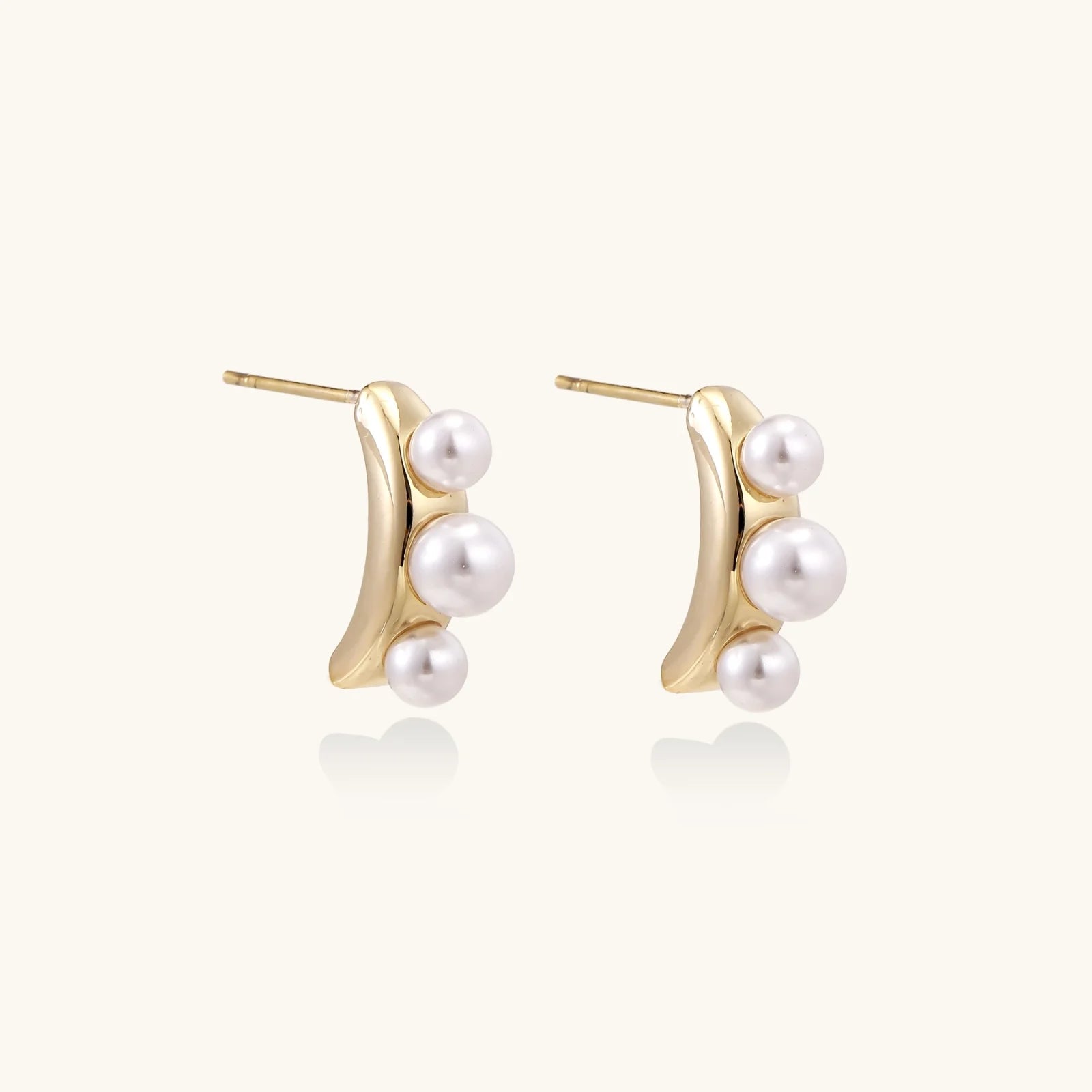 14K gold-plated curved stud earrings with three white freshwater pearls aligned vertically on cream background