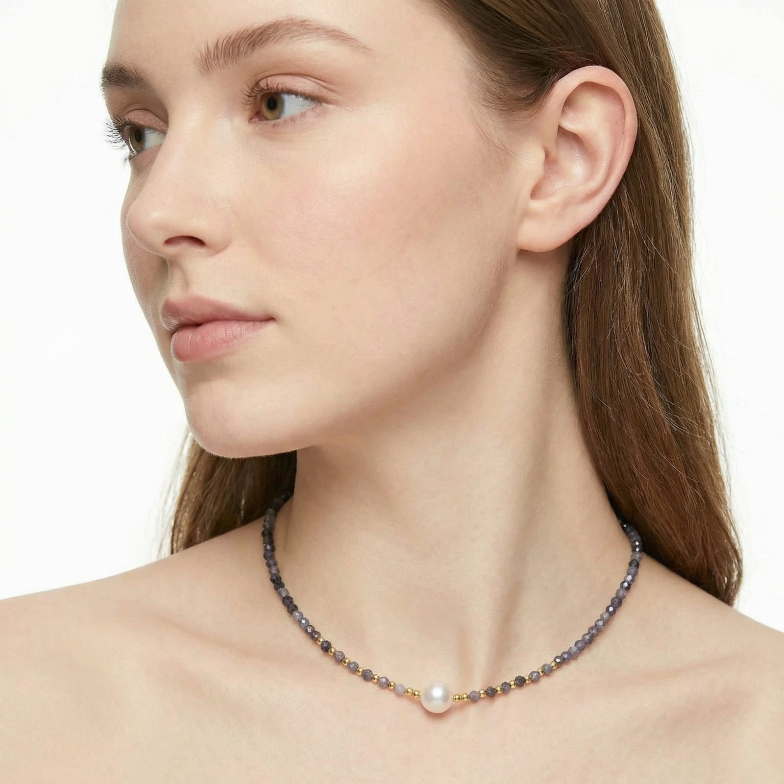 Woman wearing a delicate iolite necklace with a pearl pendant on a plain background